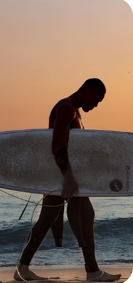 Un hombre caminando por la playa con una tabla de surf, disfrutando de la serena vista del océano y el sonido de las olas rompiendo.